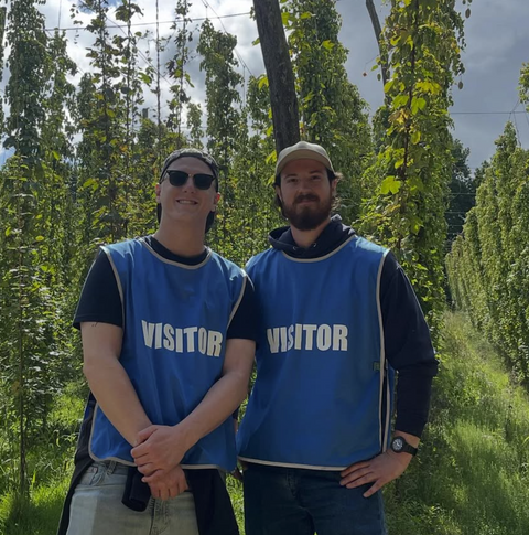Two smiling visitors in tabards among the hops at a Dorking Brewery hop-garden visit.