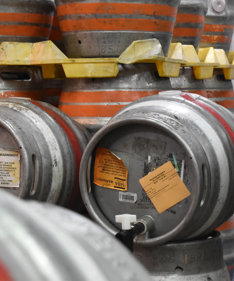 Stack of metal beer kegs with warning labels on a yellow pallet.