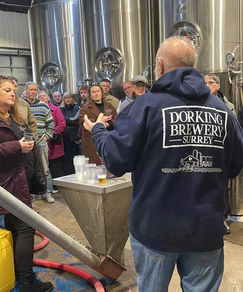 A guide leading visitors on a brewery tour at Dorking Brewery, tasting beer beside the fermentation tanks.