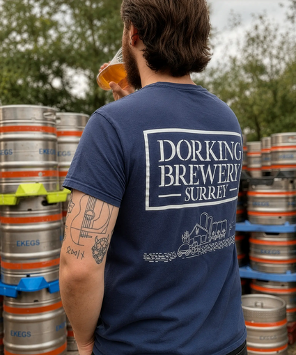 Person wearing a Dorking Brewery Surrey t-shirt in front of beer kegs.