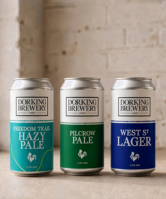 Three cans of Dorking Brewery beer on a wooden surface with a neutral background