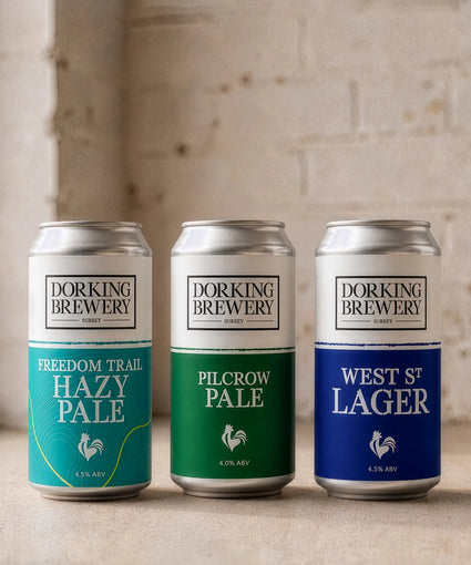 Three cans of Dorking Brewery beer on a wooden surface with a neutral background
