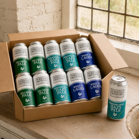 Box of Dorking Brewery beer cans on a wooden surface with a window in the background.
