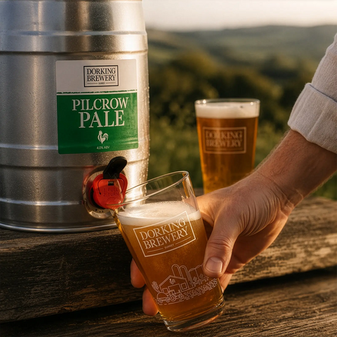 Dorking Brewery Pilcrow Pale beer keg and glass on a wooden surface with a white brick wall background.