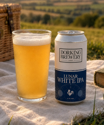 Pint of Dorking Brewery Lunar White IPA next to a can on a picnic blanket with a scenic background.