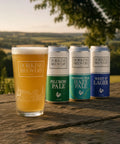 Dorking Brewery beer glass and cans on a wooden surface with a scenic background